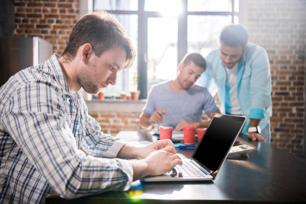 istock Young man using laptop while colleagues discussing project, small business meeting concept 677467698