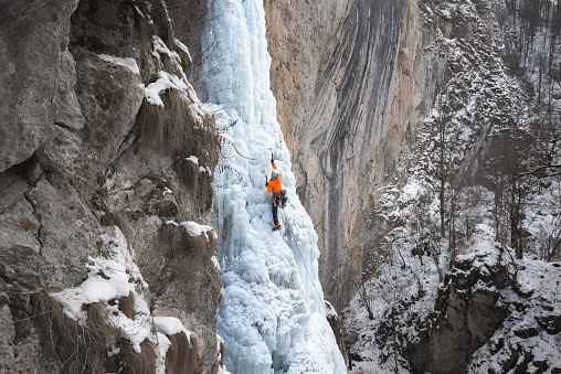 Back view of male alpinist ice climbing on steep  frozen cascade