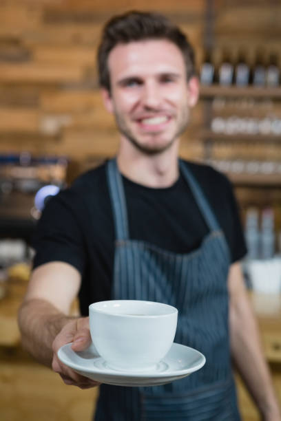 istock Smiling waiter offering cup of coffee at counter 677479066