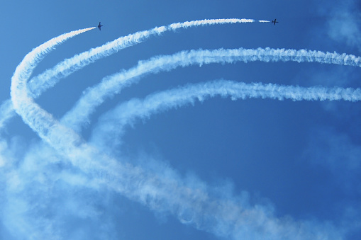 Two airplanes with smoke trails in the blue sky during air show