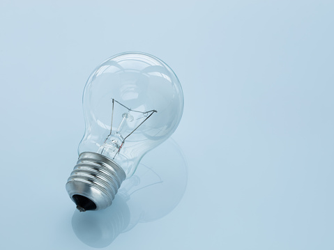 The light bulb lies on a glossy surface on a light blue background. Reflection of a light bulb.