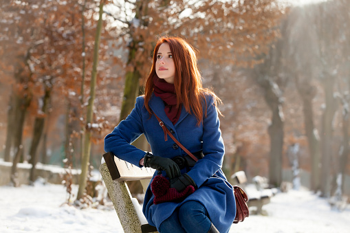 photo of beautiful young woman sitting on the bench in the park in winter
