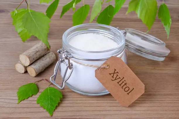 Photo of sugar substitute xylitol, a glass jar with birch sugar, liefs and wood