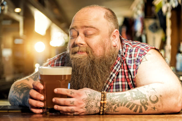 Delight bearded male drinking beverage in pub This sweet smell of fresh alcohol. Fat man showing enjoyment while tasting cold foamy ale in tap-room pub bar counter bar men stock pictures, royalty-free photos & images