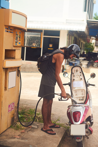 Shot of a young tourist refueling his scooter at a gas station while exploring a foreign city