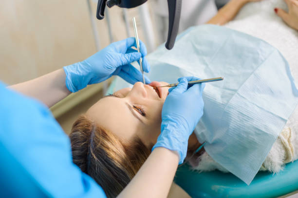стоматолог-женщина лечит caries с помощью микроскопа в кабинете стоматолога - dentists chair people care medical equipment стоковые фото и изображения
