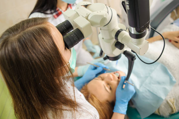 istock Female dentist treating caries using microscope at the dentist office 677581574