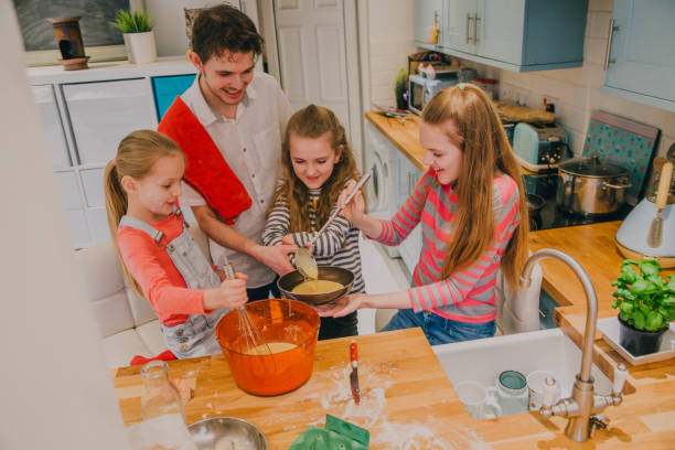 istock Father and Three Daughters Pouring the Mix into a Pan 677582624