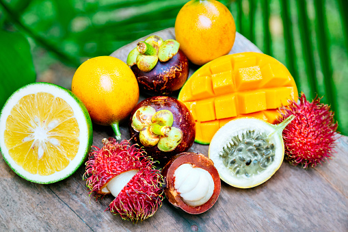 Ripe and fresh exotic fruits: Sri Lankan green orange, mangosteens, passion fruit, mango and rambutan on the wooden table and green background
