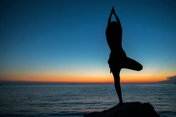istock Woman doing yoga tree pose by sea during sunset 677597676