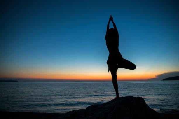 istock Woman doing yoga tree pose at beach during sunset 677597710