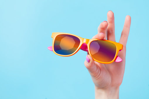 photo of female hand holding sunglasses on the wonderful blue background