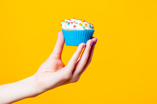 photo of female hand holding cupcake on the wonderful yellow background