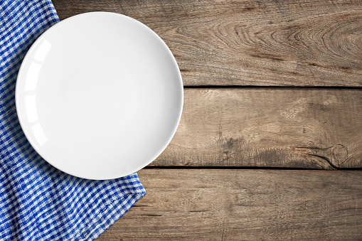 Top view of blank white dish and blue tablecloth on a wood background with copy space.