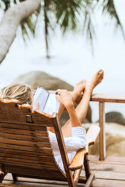 istock Young woman reading a book while relaxing on tropical island 677675696