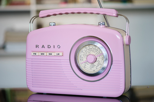 Retro looking pink radio with a round dial for frequencies and buttons for wavelengths selection.