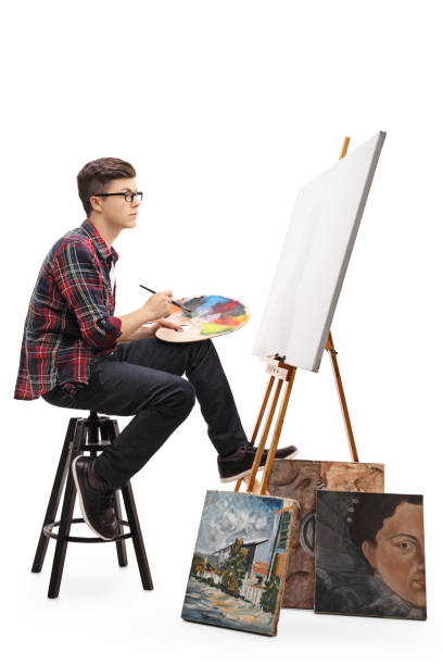 istock Teenage painter with paintbrush and palette looking at canvas 677698404
