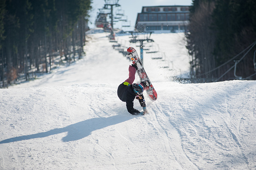 Snowboarder in the moment of falling on the snowy slope overlooking a ski lifts and a ski run at a winter resort, extreme sport