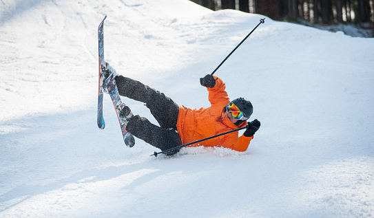 Skier fell in snow during the descent from mountain. Male is wearing orange jacket, helmet and goggles. Carpathian Mountains, Bukovel