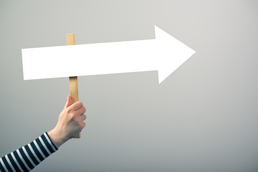 Woman holding guiding direction arrow sign in hand, concept of guidance and decision making