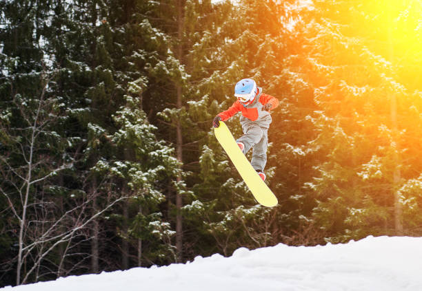 Boy jumping and keeps one hand on the snowboard in the mountains with snow-covered firs in background, extreme sport