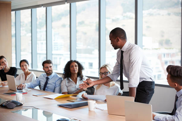istock Businessman Stands To Address Meeting Around Board Table 677809664