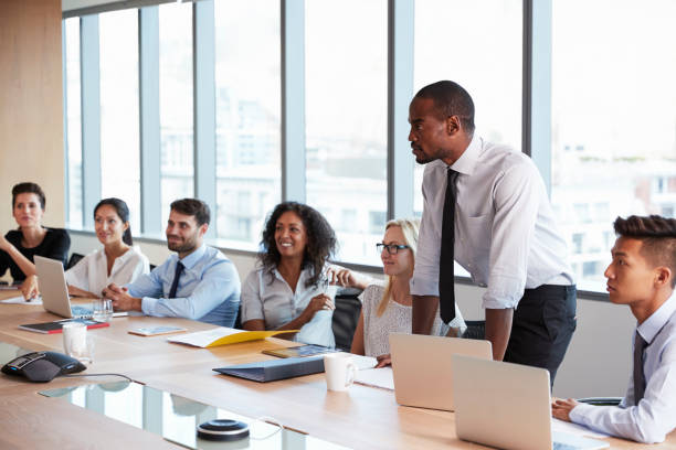 istock Businessman Stands To Address Meeting Around Board Table 677809680