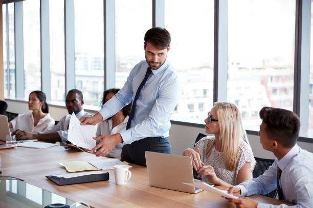 istock Businessman Stands To Address Meeting Around Board Table 677809692