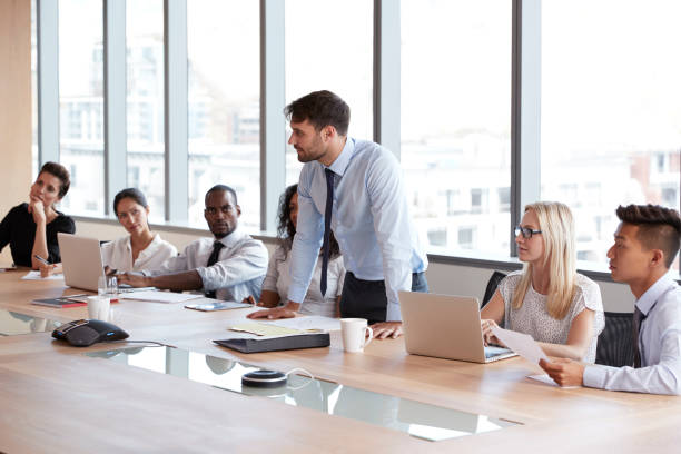 istock Businessman Stands To Address Meeting Around Board Table 677809710