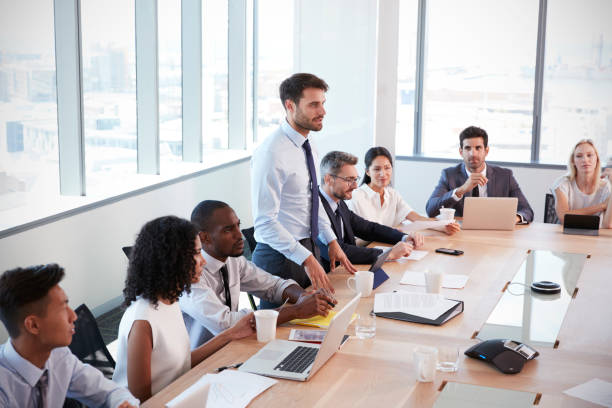 istock Businessman Stands To Address Meeting Around Board Table 677809768