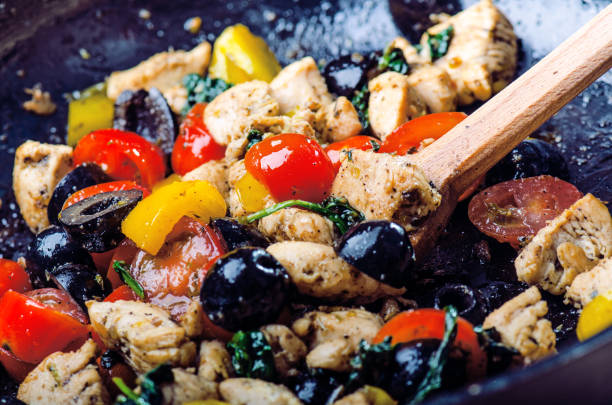 cooking of food on a pan. olive, cut chicken breast, tomatoes, chilly, pepper, spinacy and herbs - cooking oil olive oil nutritional supplement spoon imagens e fotografias de stock