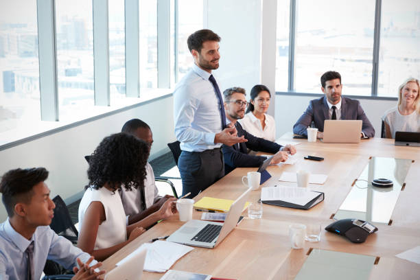 istock Businessman Stands To Address Meeting Around Board Table 677809808