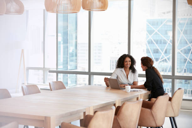 Two Businesswomen Using Laptop In Boardroom Meeting Two Businesswomen Using Laptop In Boardroom Meeting looking down photos stock pictures, royalty-free photos & images