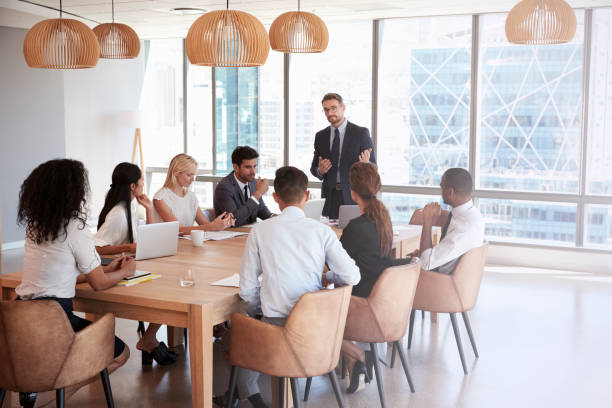 istock Businessman Stands To Address Meeting Around Board Table 677809952