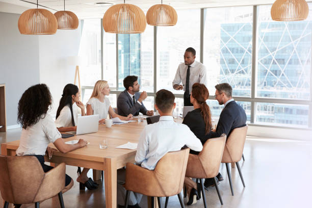 istock Businessman Stands To Address Meeting Around Board Table 677809970