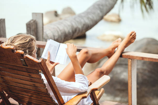 istock Young woman reading a book while relaxing on tropical island 677823096