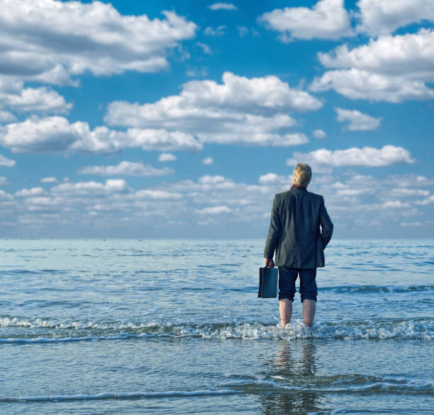 istock Businessman barefooted at water´s edge by the sea getting away from it all 677845224