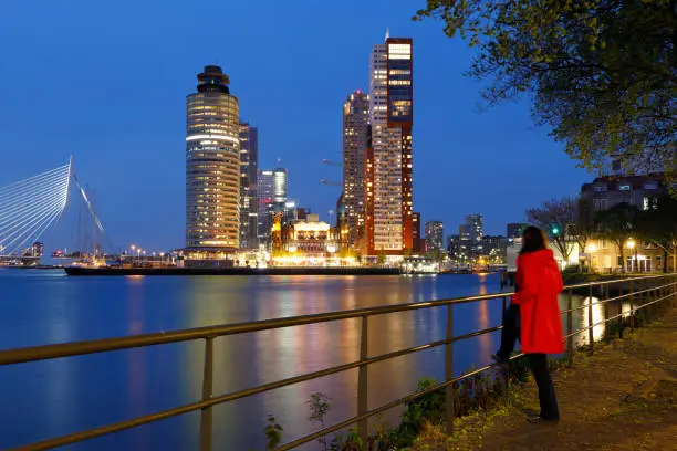 Young woman regarding the illuminated Wilhelminapier skyline at Rotterdam, The Netherlands