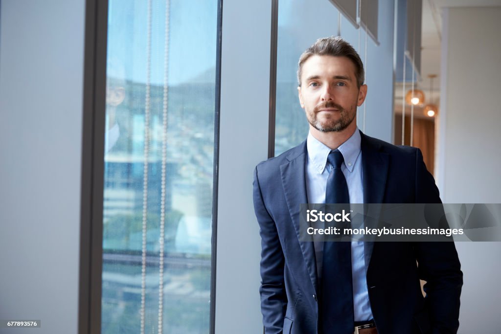 Portrait Of Businessman Standing By Window In Office Men Stock Photo