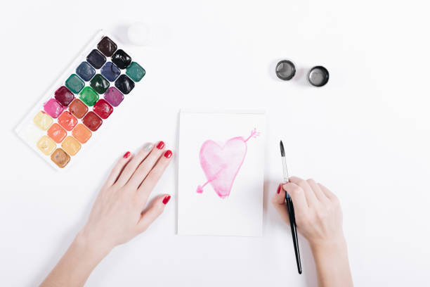 Female hands drawing with watercolors pink heart, top view
