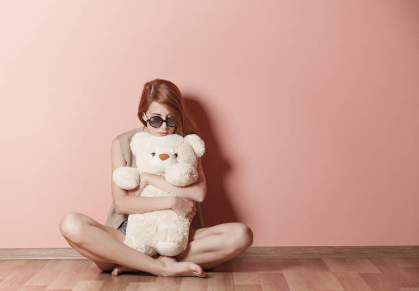 photo of beautiful young woman hugging teddy bear and sitting near the wall photo of beautiful young woman hugging teddy bear and sitting near the wall woman teddy bear stock pictures, royalty-free photos & images
