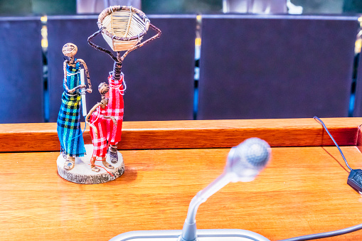 An african ethenticity craft figurine with three people together listening to the speaker or judge with a microphone.