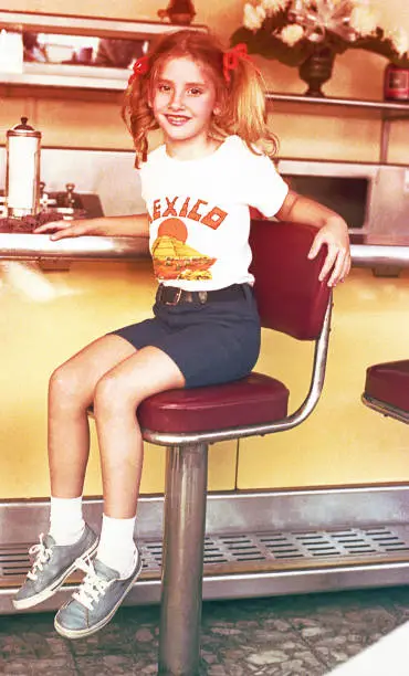 Vintage photo from the eighties featuring a girl sitting in a dinner.