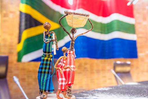 An african ethenticity craft figurine with three people together standing at the conference or boardroom with the south african flag in the background.