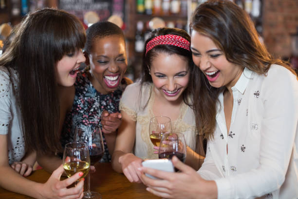istock Happy female friends with wineglasses using mobile phone 677975524