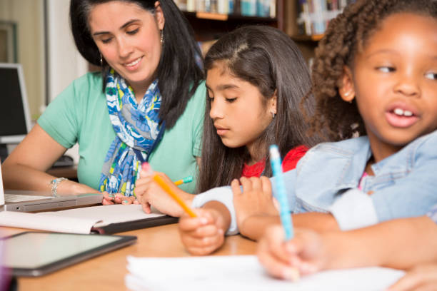 istock Teacher, mentor helps elementary-age schoolgirls with homework. 678077804