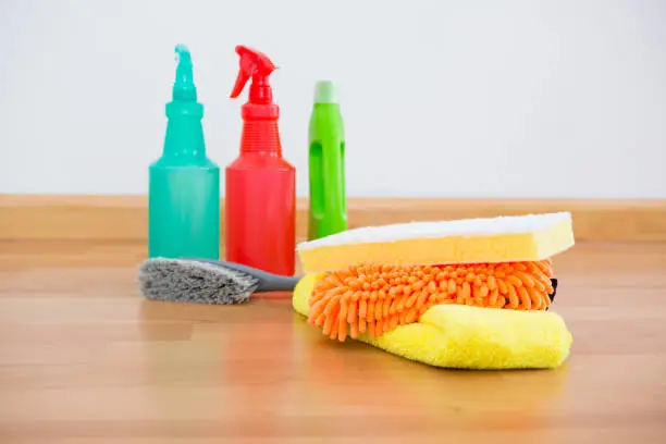 Close up cleaning sponge and chemical bottles on hardwoodfloor