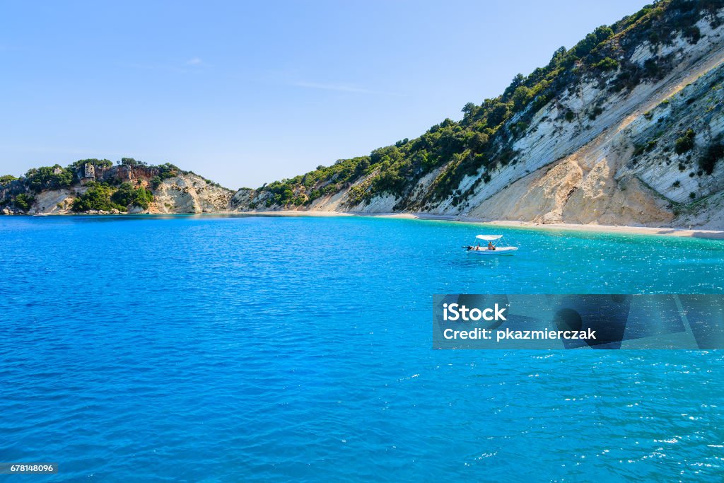 Small boat on azure sea with beautiful beach on coast of Ithaca island, Greece Kefalonia is a Greek island in Ionian Sea. It is the largest of Ionian islands and the sixth largest Greek island. Kefalonia Stock Photo