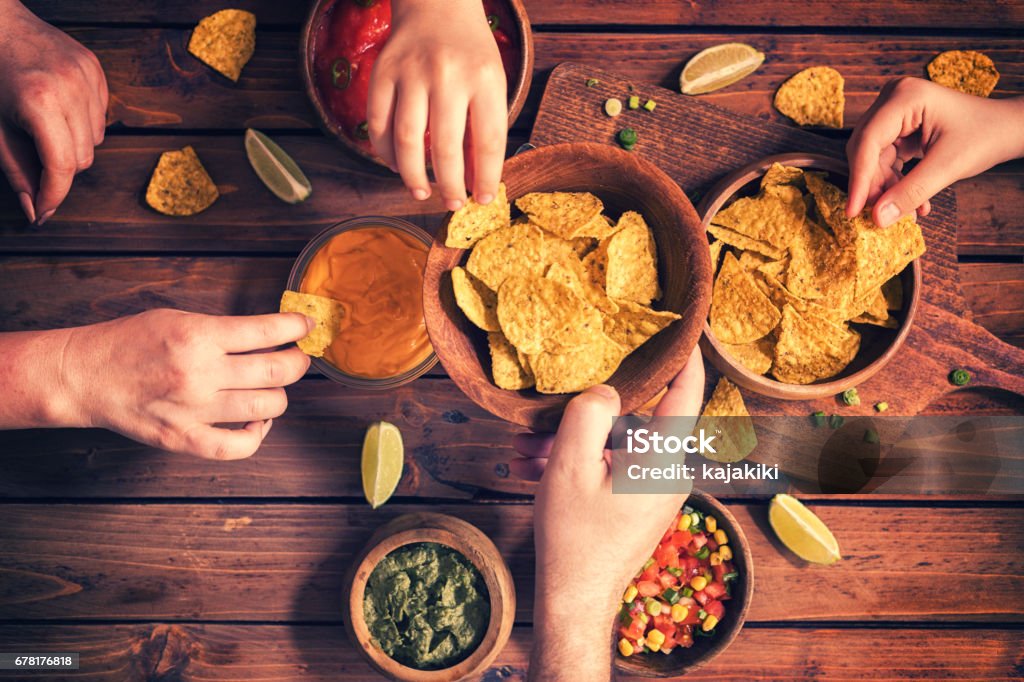 Family Eating Nachos With Sauces Family eating nachos with homemade sauces Snack Stock Photo