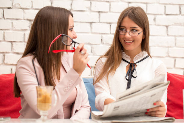 istock Two young women flipping through newspaper and talk 678210260